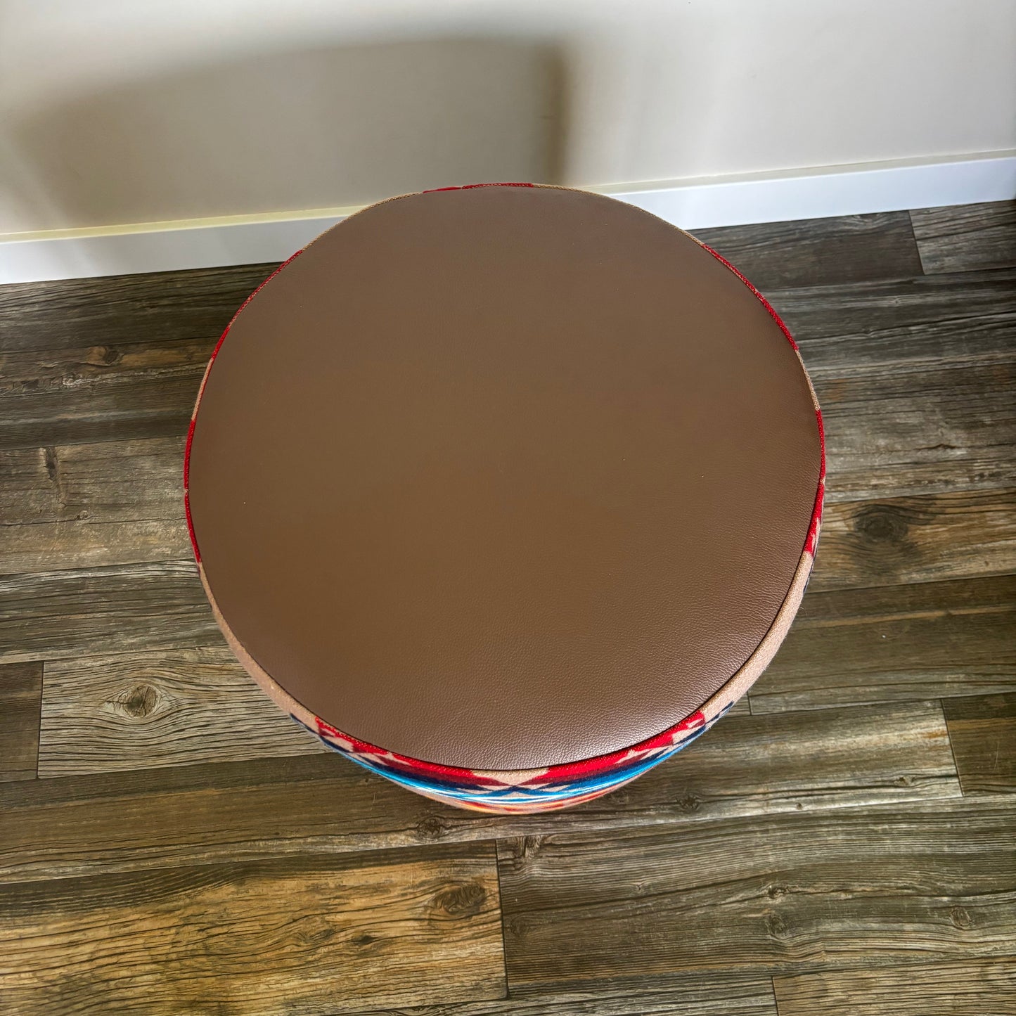 Alt: Top-down view of ottoman showing brown leather surface and partial colorful fabric sides.