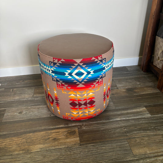 Front view of round ottoman featuring geometric Pendleton fabric and smooth leather top, placed indoors.