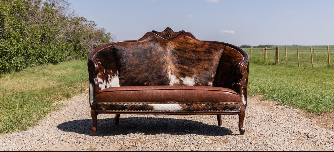 Cowhide-patterned sofa on a gravel path with greenery and a fence in the background