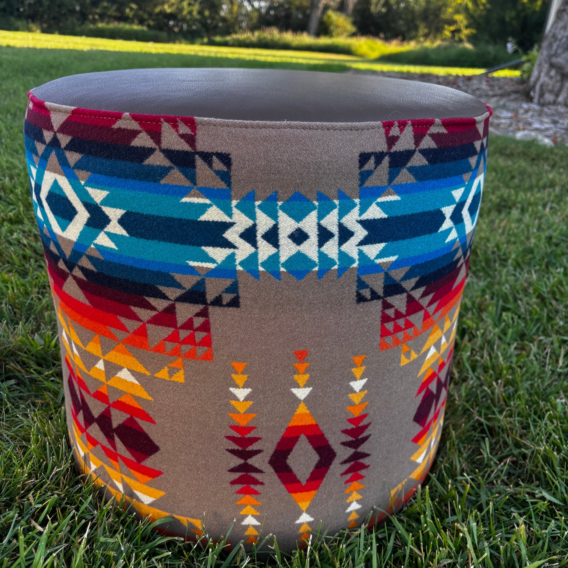 Close-up outdoor view of Pendleton fabric pattern on ottoman, with grass and trees in background.