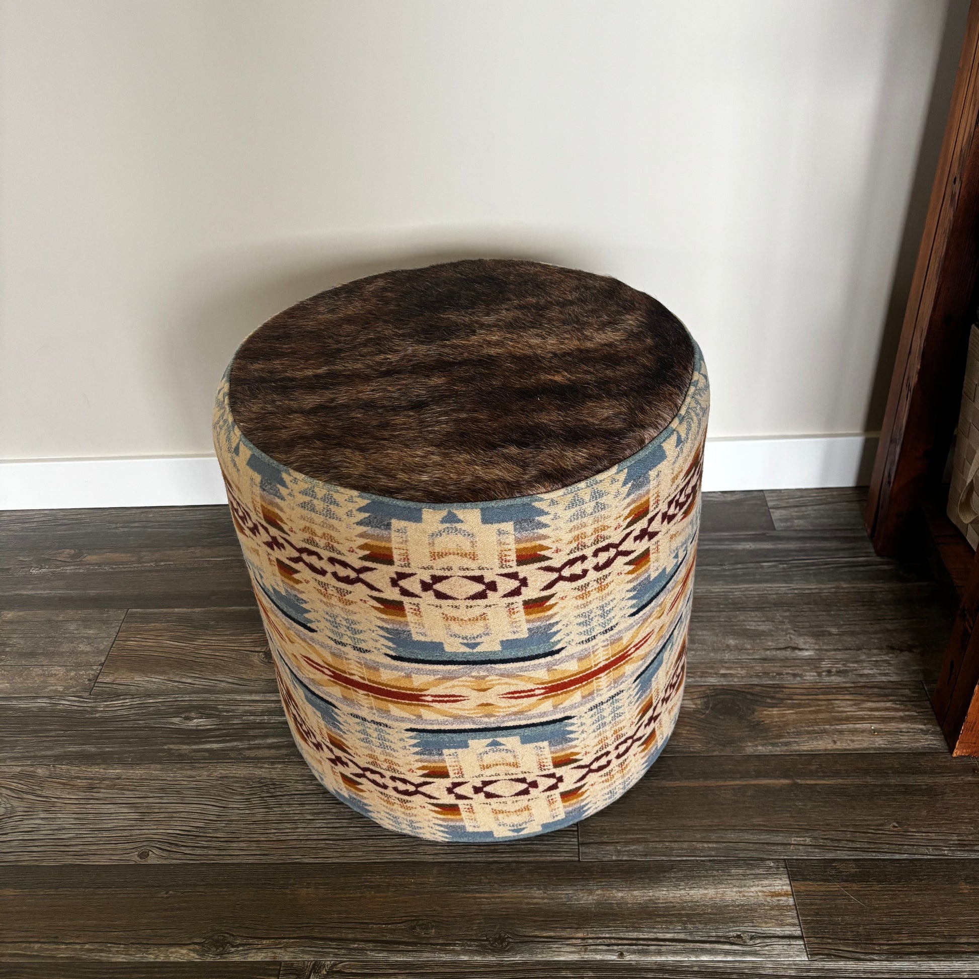 Handmade round ottoman with Pendleton Shonto Wheatlands fabric and genuine hair-on-hide top, placed on wooden floor