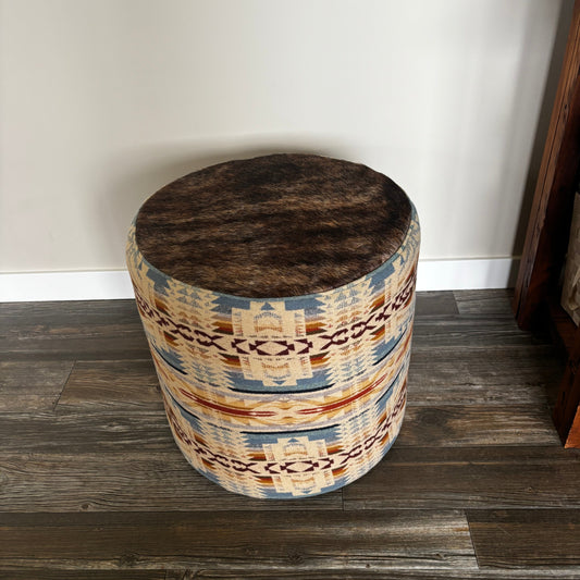 Handmade round ottoman with Pendleton Shonto Wheatlands fabric and genuine hair-on-hide top, placed on wooden floor