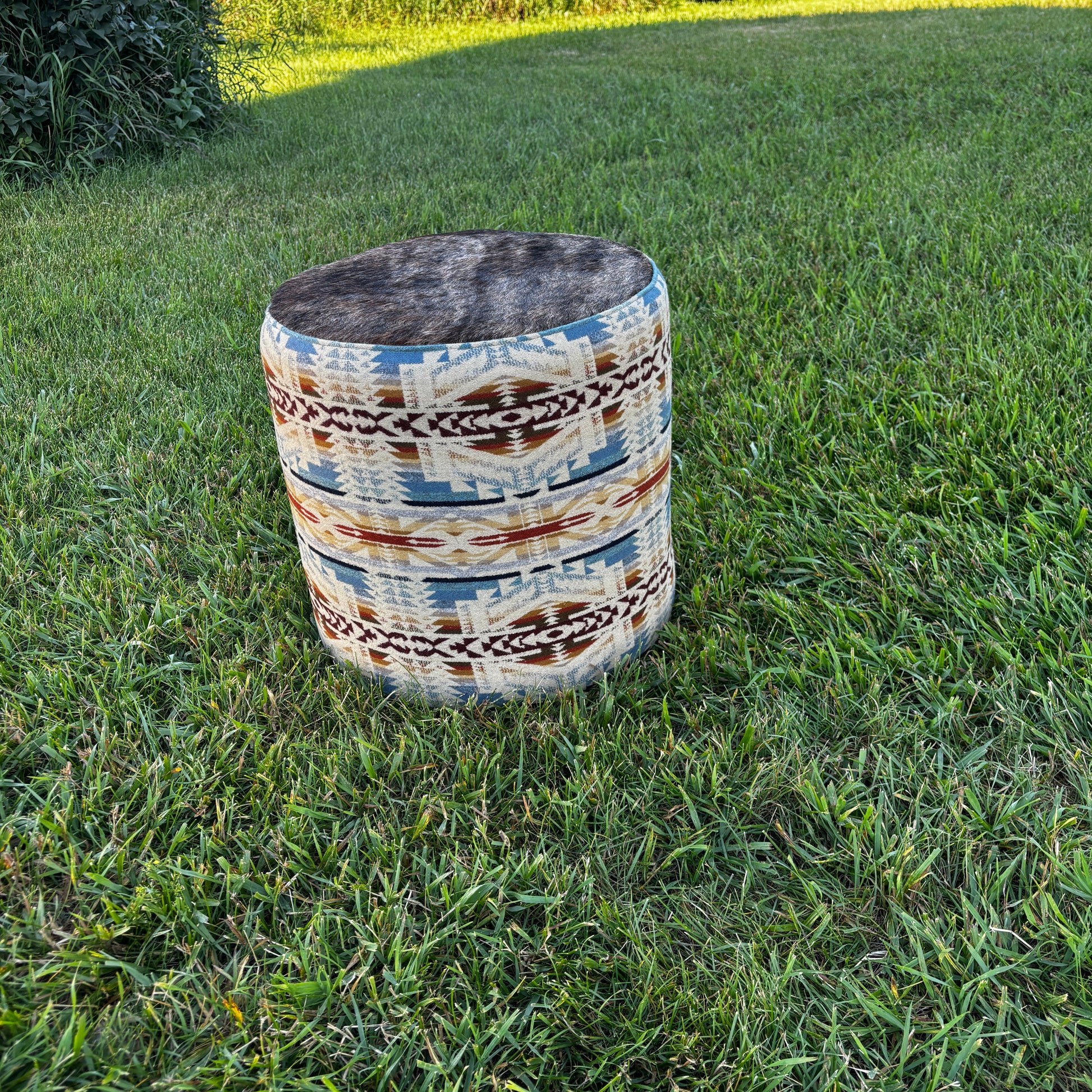 Ottoman outdoors on green grass, highlighting hair-on-hide top and colorful Pendleton fabric.