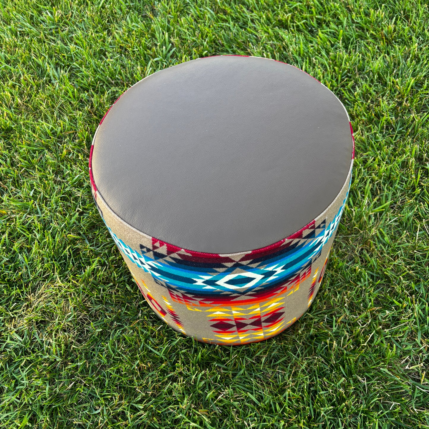 Overhead view of ottoman on grass highlighting smooth leather top and vibrant fabric design.