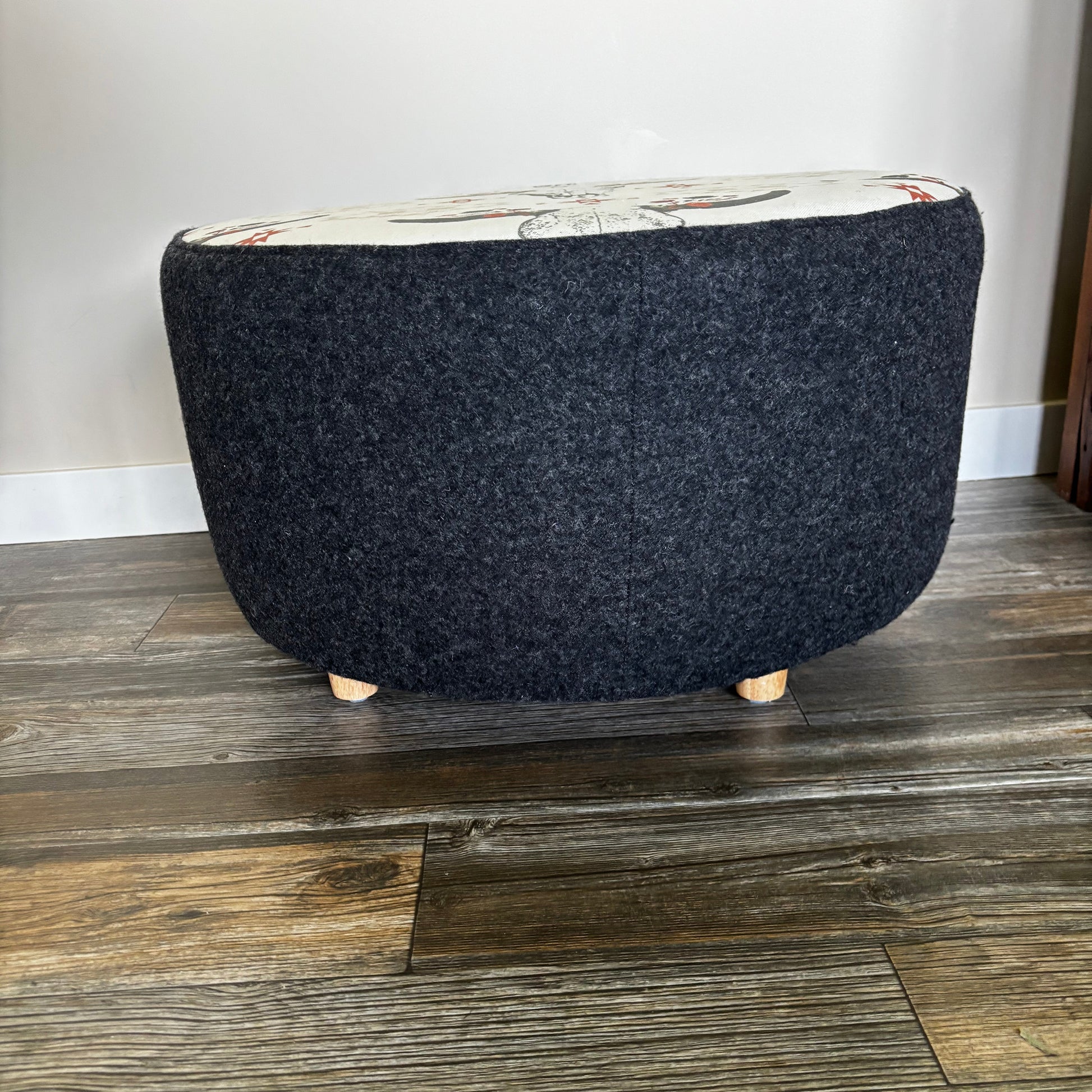 Rear view of the ottoman showing black wool sides and wooden feet