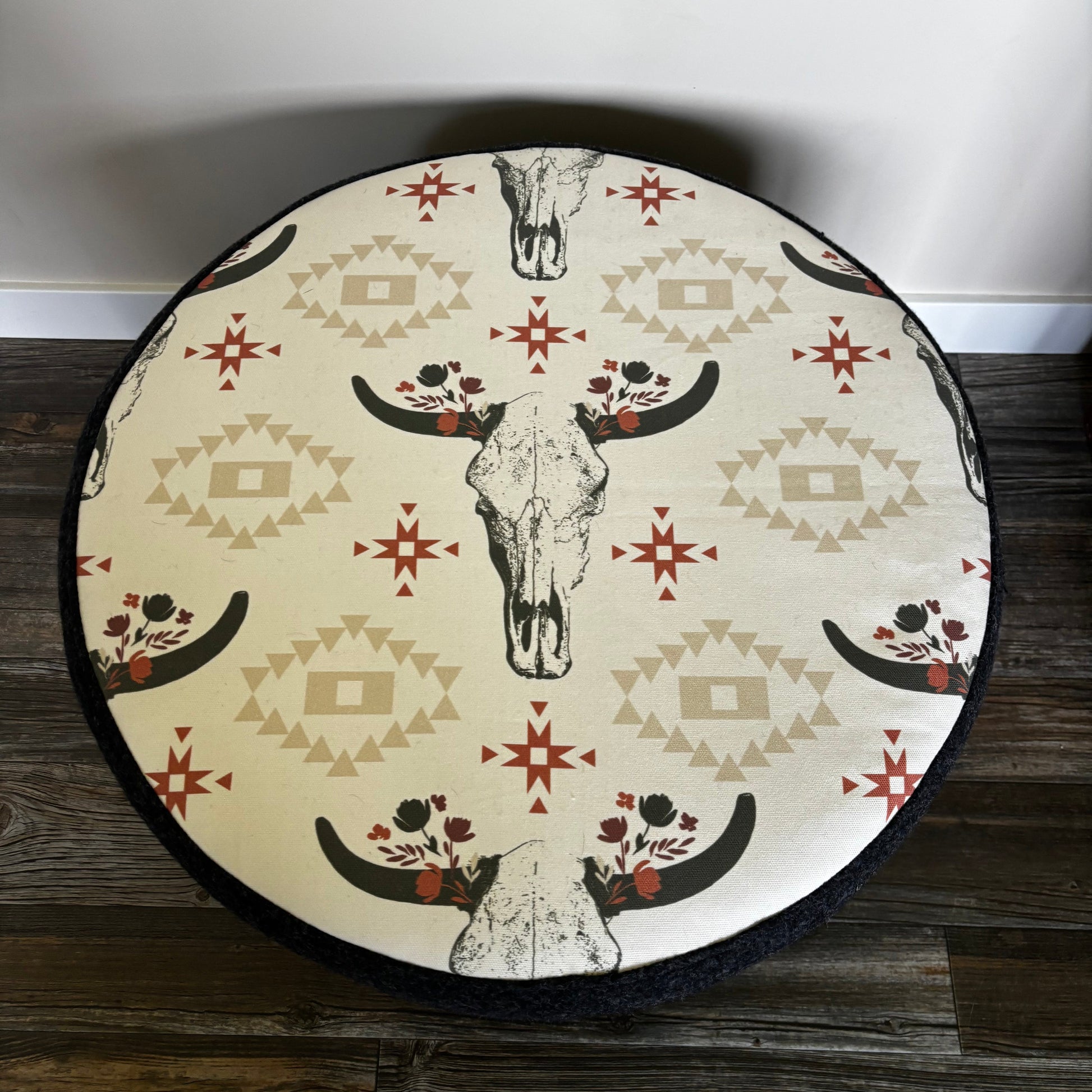 Top view of handmade ottoman with cow skull print and black wool sides, sitting on dark wooden flooring