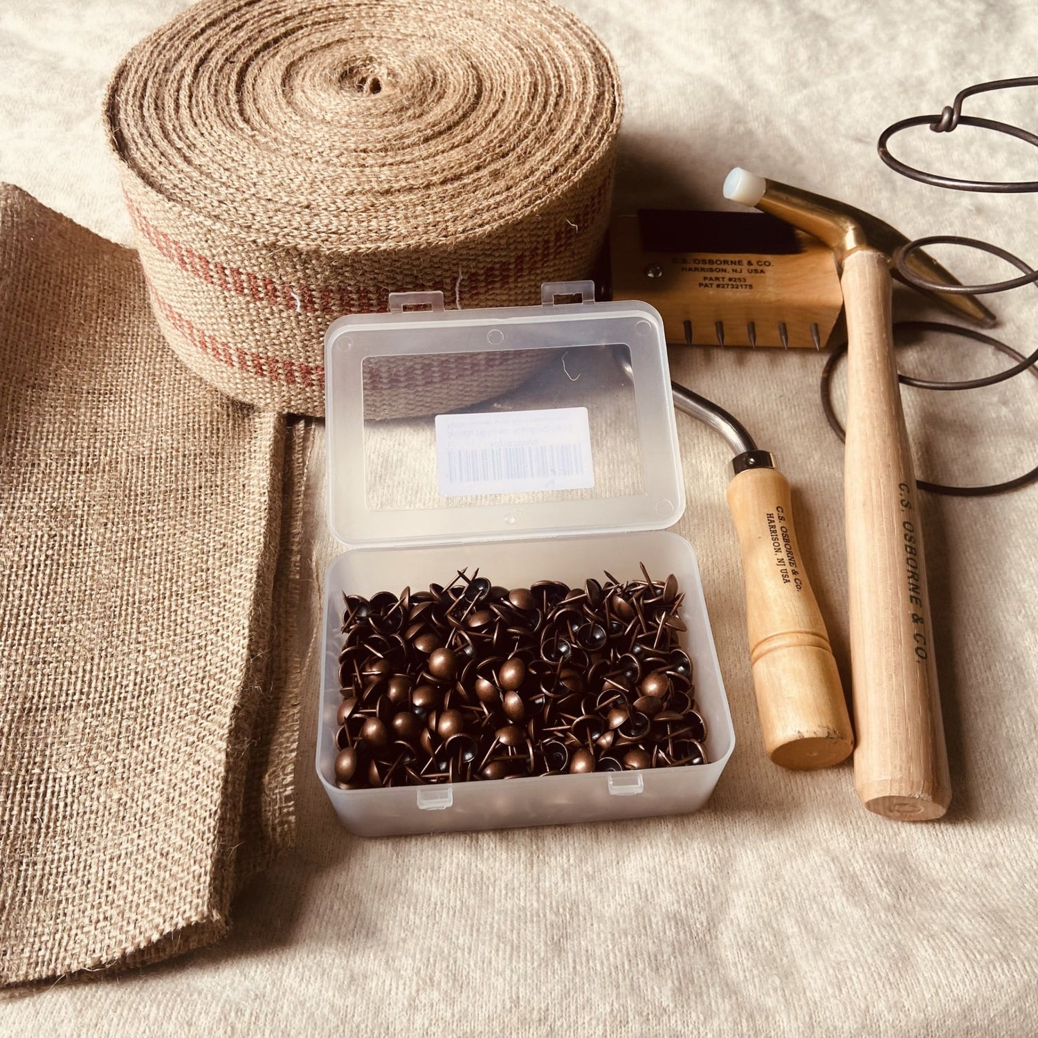 Box of nails, roll of burlap, and tools on a textured surface